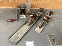 Three antique hand planes and a grinding wheel arranged on a workbench.