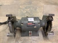 Front view of entire Shopcraft bench grinder with grinding wheel, wire brush, protective shields, and power switch.