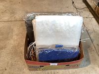 Box containing assorted polyethylene tarps of various sizes and colors including blue, white, and silver.