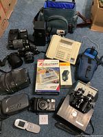Overview of lot items including Contax camera, lenses, binoculars, telephone, Kodak flash box, Diesel programmer box, cell phone, and clock radios.