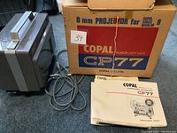 Photo of the Copal Sekonic CP77 8mm film projector, its original box and instruction manual on floor.