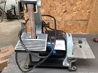 Front view of the sander showing vertical sanding belt, ribbed metal table, on/off switch, dust port
