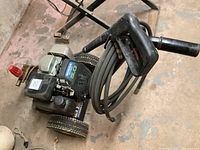 Pressure washer unit front angle showing Honda 5.0hp engine, steel frame, wheels, hose and spray gun