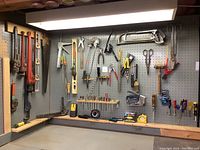 Overall view of pegboard with various hand tools arranged for sale including pipe wrenches, levels, saws, pliers, and small hand tools.