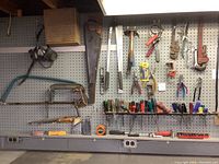 Wide view of pegboard showing various saws, clamps, pliers, screwdrivers, and a measuring tape arranged on shelves and hooks.