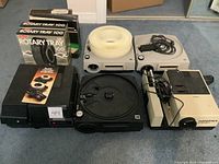 Full view of all slide projectors and rotary trays arranged on floor including Kodak Carousel 1600, Hanimex 1202, and three Rotary Tray 100 boxes.