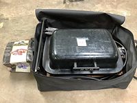 Compact propane grill inside black carrying bag with box of briquettes on the side