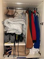 Closet with hanging sweaters and jackets, folded blanket, wooden hangers, and pair of grey and black boots with yellow details.
