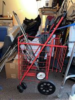Red metal wire mesh pull cart with wheels shown among various household items.