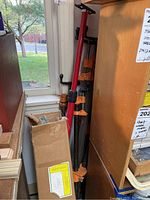 Pipe clamps with orange parts and metal pipes stored near a window and cardboard box.
