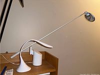Two white adjustable desk lamps on a wooden surface showing the base and long arms.