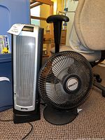 View of both the silver Intertek heater and black Lasko fan side by side on a carpeted floor near storage bins.