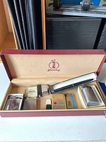 Five assorted lighters and a pen-shaped metallic case inside a Spalding lined box