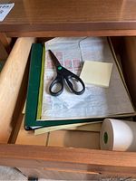 Photo of drawer containing scissors, sticky notes, and white label roll.