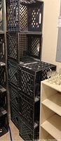 Stack of black plastic milk crates, some connected by duct tape, showing wear and scratches.