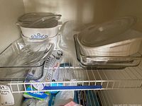 Shelf display of assorted glass and Corning Ware bakeware including clear glass baking dishes and Corning Ware casserole dishes with lids