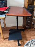 Side view of rolling desk showing wood finish top, black metal base with wheels, and CPU shelf at bottom.