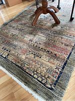 Close-up photo showing the rug under a wooden table leg, highlighting the intricate multi-patterned design and fringed edge.