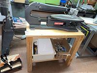 Craftsman scroll saw mounted on wooden two-tiered table with hardware storage below