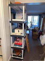 Front angled view of plastic shelf with various miscellaneous boxes and items on the shelves, in basement area.
