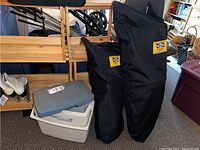 Two black zippered carry bags with yellow Atlas Snow-Shoe Company logos next to a gray and white Coleman cooler.