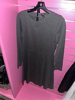 Gray long-sleeve dress hung on black hanger against pink background.