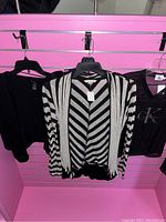 Three medium size women's tops hanging on hangers, including a black cardigan, black and white striped cardigan, and black Calvin Klein mesh top.