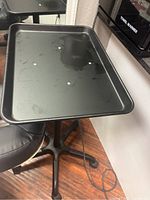 Photo showing a black rectangular rolling tray with raised edges on a rolling stand.