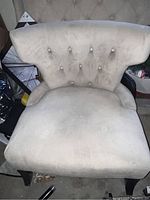 Photo showing front view of the light beige fabric upholstered chair with button tufting and dark wooden legs.