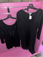 Black dress and black top hanging on hangers against pink slatwall background.