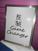 Single photo of a 12x8 framed picture with motivational phrase 'Be The Game Changer' in black text on white background, silver metallic frame.