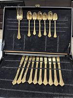 Partial set of gold plated flatware displayed inside a carrying case showing a serving fork, six teaspoons, and six butter knives.