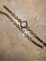 Photo showing a wristwatch and matching bracelet laid flat on a marble surface, both featuring linked circular metal elements.