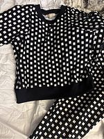 Full view of the matching top and pants laid flat, showing the black and white geometric print.