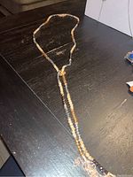 Full view of the necklace laid flat showing alternating metallic silver, gold, and cream beads, and the dual-strand drop pendant.