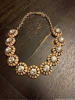 Photo of a short gold-tone chain necklace with ten large clear rhinestones encased in petal-shaped settings laid out on a wooden surface.
