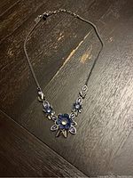 Necklace laid flat displaying blue topaz stones in floral settings and silver-tone chain on dark wooden surface.