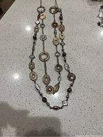 Photo of a mixed-metal long necklace with various textured and shaped metal charms and alternating beads spread on a white surface.