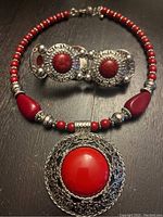 Photo showing matching red stone necklace with large pendant and bracelet with ornate silver-tone settings and red stones.