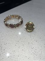 Photo showing a matching ring and bracelet placed on a white surface. The ring has a central oval stone with two clear side accents, and the bracelet has linked oval stones in gold-tone metal.
