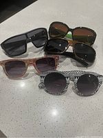 Photo of five pairs of sunglasses on a countertop with various frame styles and lens colors