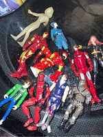 Top-down photo showing 11 small action figures including Iron Man and G.I. Joe characters, laying on a dark surface.