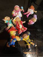 Photo showing seven vintage Cabbage Patch Kids figurines in various colorful outfits and poses on a black surface.
