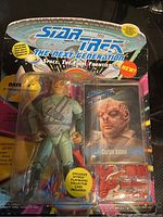 Photo showing carded Captain Gidom action figure from Star Trek The Next Generation series with accessories and collector's card inside sealed blister packaging.