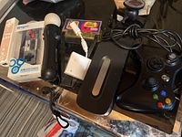 Overall view of the gaming controllers and accessories on a surface including PS Move controller, Xbox controller, Biogenik Wireless Classic controller, Wii Remote, Game Genie, and cables.