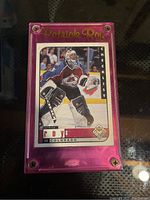 Photo of Patrick Roy hockey card in a pink clear protective case showing the card with Patrick Roy in Colorado Avalanche uniform.