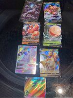 Photo showing 7 holographic Pokémon cards in protective sleeves on a dark surface.