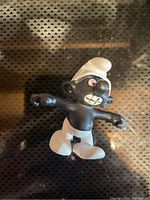 Single black Smurf figurine by Schleich with white pants and hat, displayed on dark patterned surface.