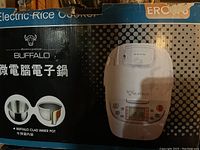 Box and front view of Buffalo electric rice cooker, highlighting digital control panel and clad inner pot illustration on packaging.