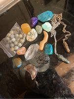 Photo of a variety of polished stones, raw crystals and two silver chains with pendants arranged on a dark surface